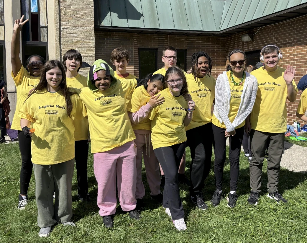 Smiling Insightful Minds students in matching yellow shirts outside on the campus lawn